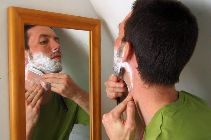 shaving with straight razor in front of mirror